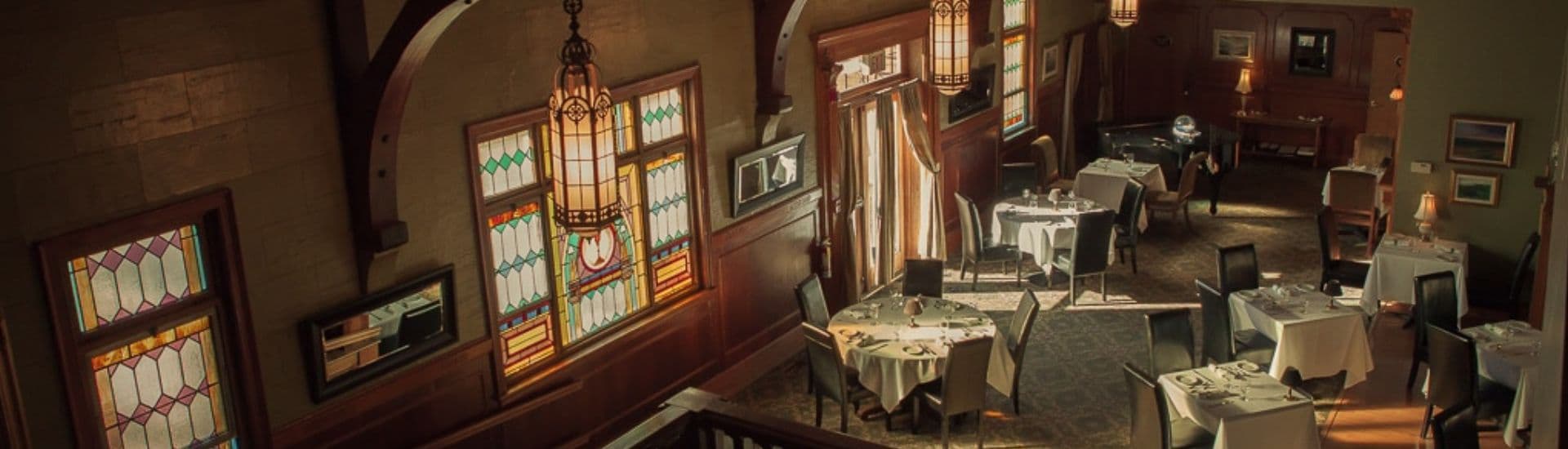 A view of an elegant restaurant interior featuring stained glass windows, chandeliers, and neatly set tables.