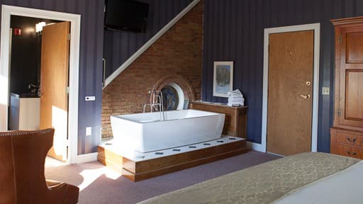A stylish hotel room featuring a modern bathtub, a cozy armchair, and decorative walls.