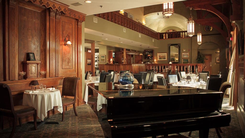 Elegant restaurant interior featuring a grand piano, wooden accents, and tables set with white tablecloths.