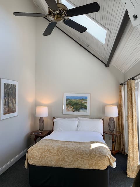 A cozy bedroom featuring a bed, two bedside lamps, artwork on the walls, and a ceiling fan.
