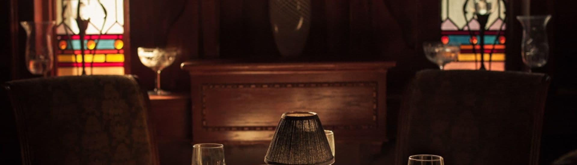 A dimly lit dining room with stained glass windows and a table set for dinner.