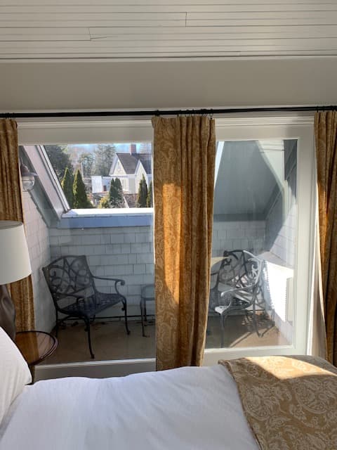 A cozy bedroom window view showcasing a small balcony with two chairs and golden curtains.