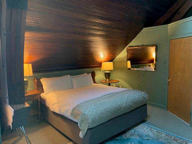 A cozy attic bedroom featuring a double bed, bedside tables with lamps, and a mirror on the wall.