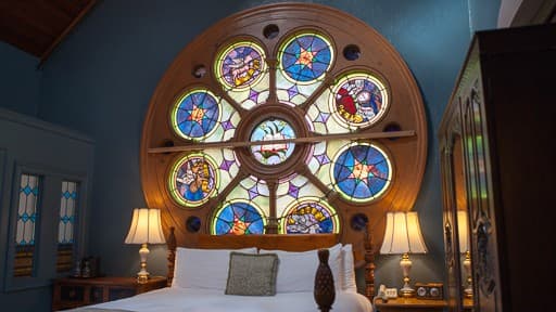 A cozy bedroom featuring a large, colorful stained glass window above the bed.