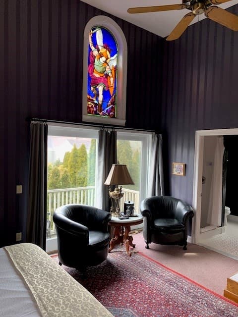 A cozy room featuring black armchairs, a side table with a lamp, a stained glass window, and dark striped walls.