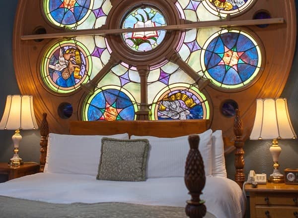 A cozy bedroom featuring a large stained glass window and elegant bedside lamps.
