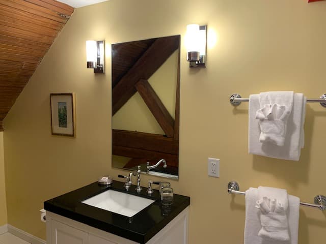 A cozy bathroom with a sink, mirror, and two neatly hung white towels against a yellow wall.