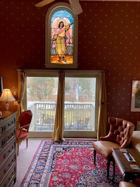 A cozy room featuring a stained glass window, a plush chair, and a view of a balcony.