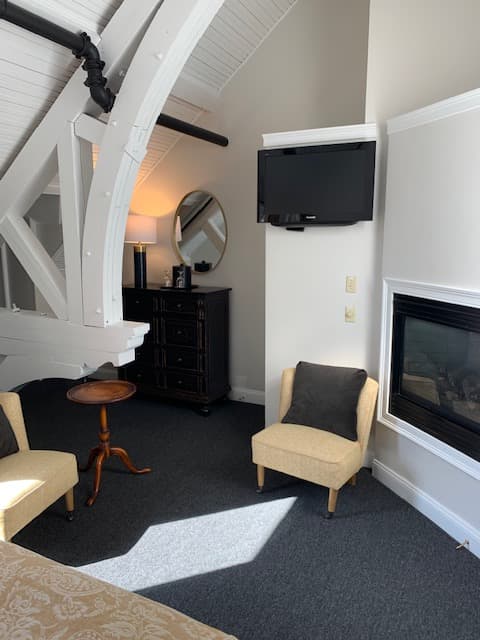 Cozy living space featuring two armchairs, a small table, a dresser, a mirror, a wall-mounted TV, and a fireplace.