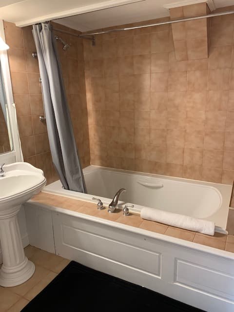 A bathroom featuring a bathtub with a gray curtain, a pedestal sink, and beige tiled walls.