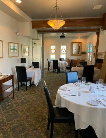A cozy dining room featuring elegantly set tables and decorative stained glass windows.