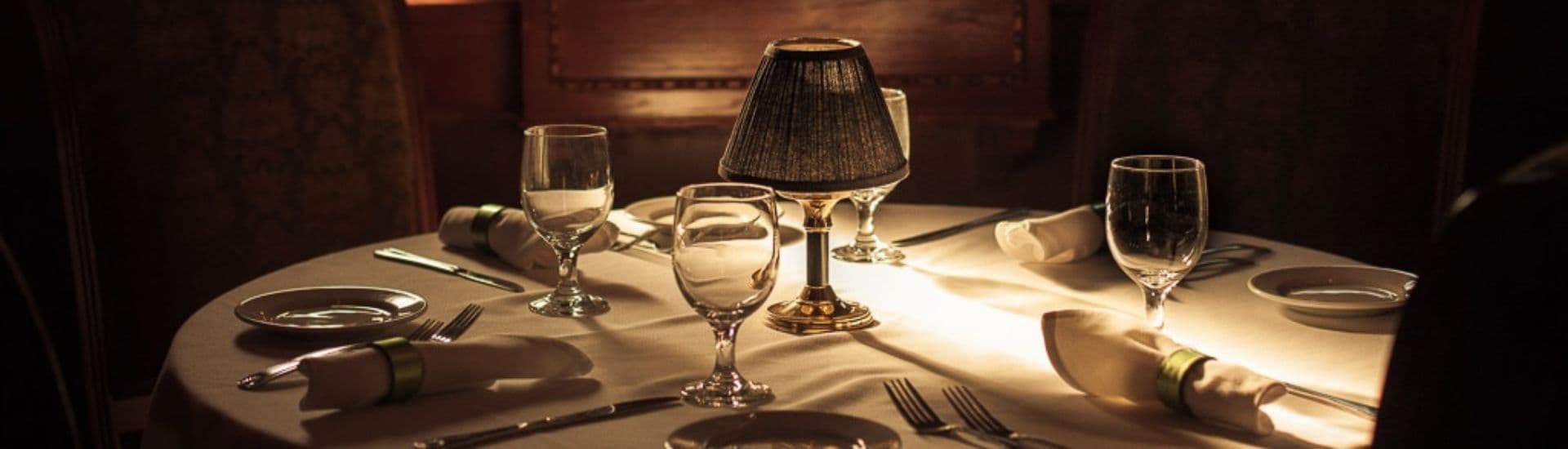 An elegantly set dining table with a small lamp, glassware, and silverware.