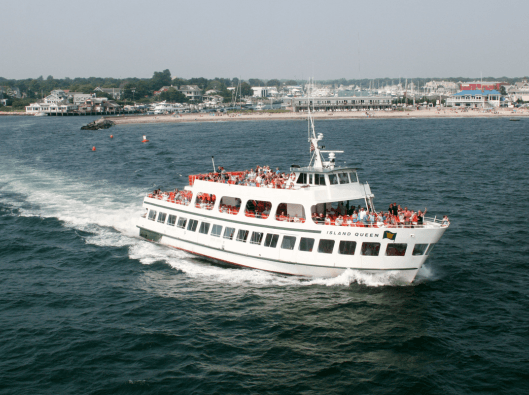 A ferry named "Island Queen" with passengers on board navigates through the water near a coastal town.