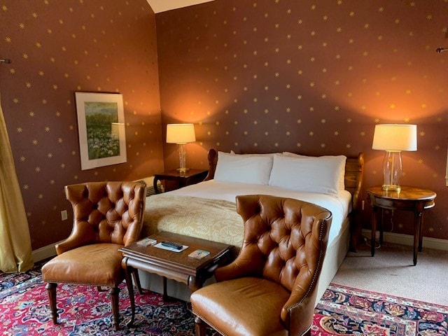Cozy hotel room featuring a queen bed, two armchairs, and warm lighting against a patterned wall.