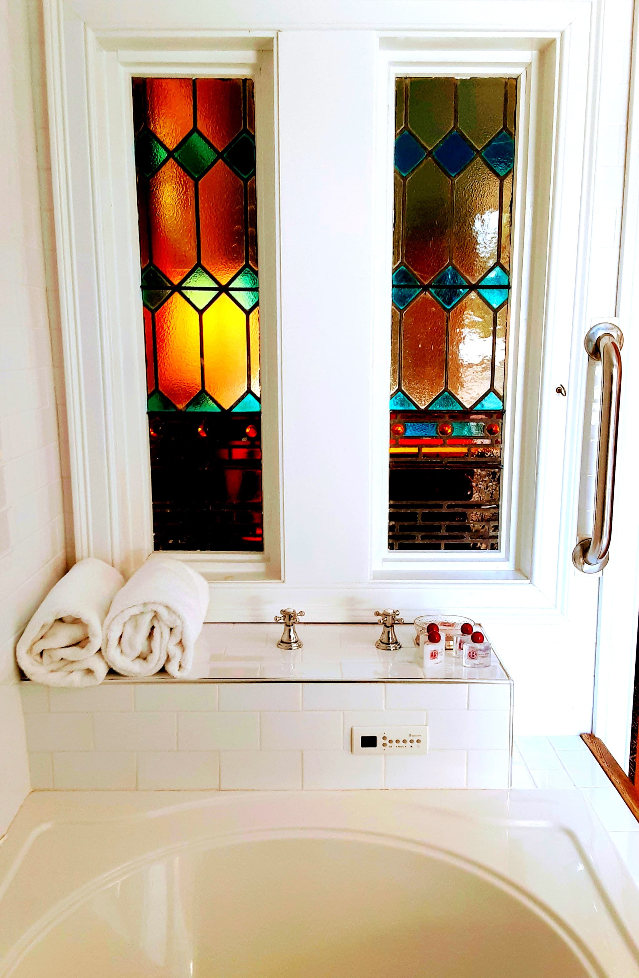 A bright bathroom featuring stained glass windows, neatly stacked towels, and a sink with toiletries.