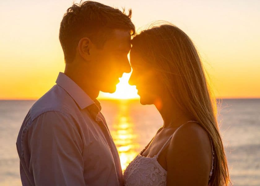 A couple gazes at each other against a sunset backdrop over the ocean. A couple gazes at each other against a sunset backdrop over the ocean.