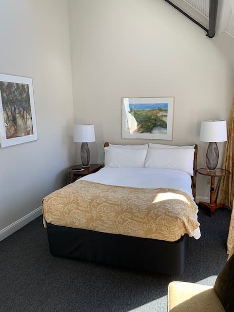 Cozy bedroom featuring a double bed, two lamps, and artwork on the wall.
