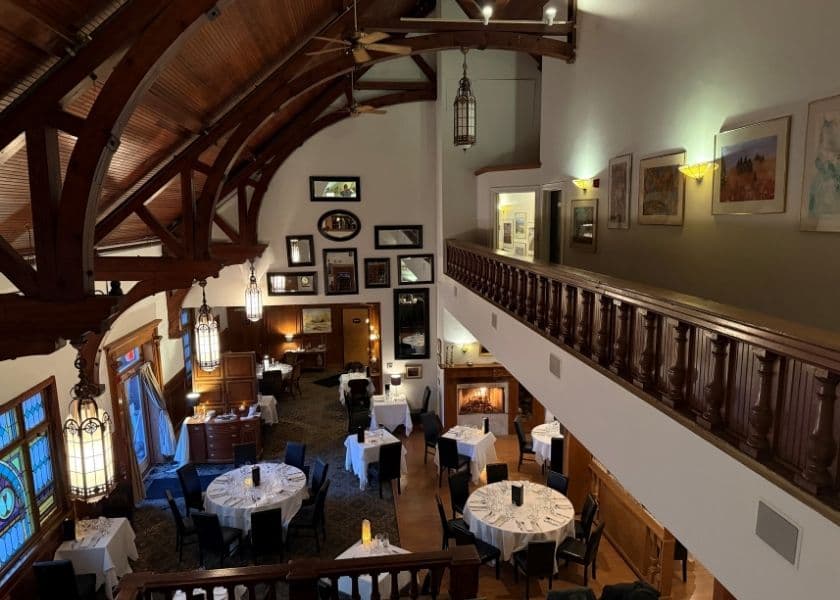 Elegant dining room at Belfry Inn, with white tablecloths, a fireplace, and high vaulted wood-beam ceilings.