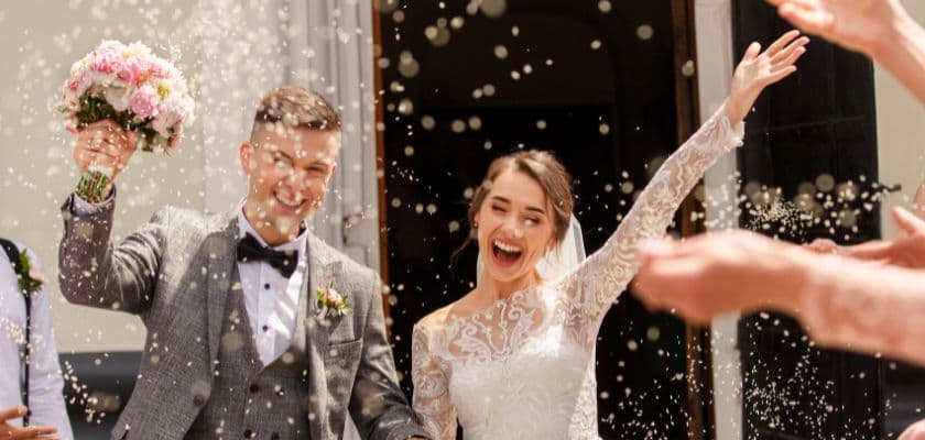 Bride and groom celebrating on their wedding day while rice is being thrown, and guests are cheering