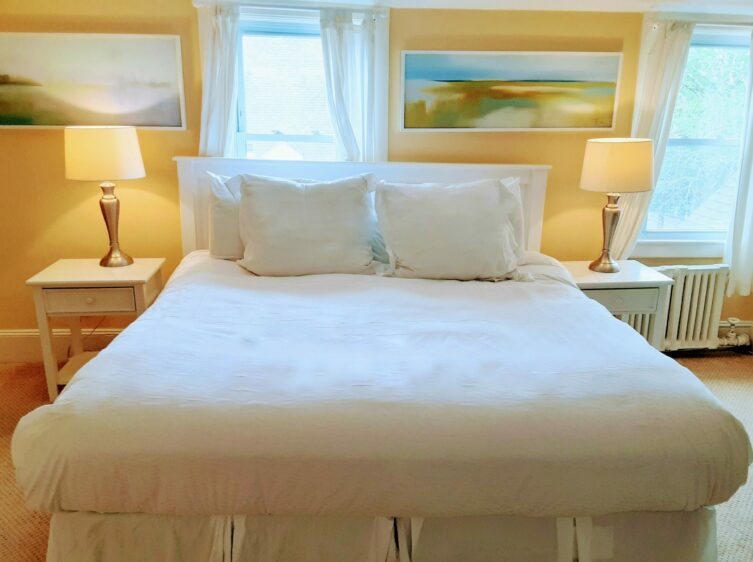 A queen bed is with 2 bedside tables with lamps and a painting