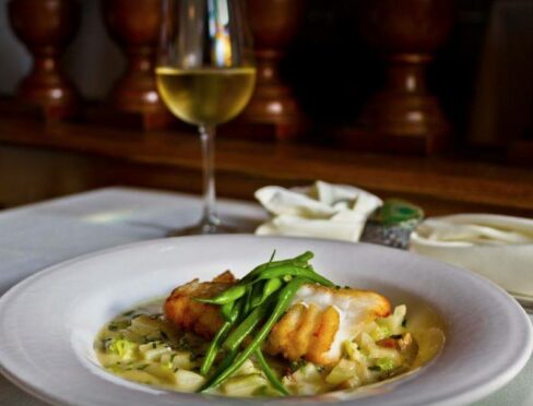 A filet of seared fish rests over a bed of risotto and is topped with green beans.