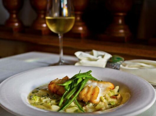 A filet of seared fish rests over a bed of risotto and is topped with green beans.