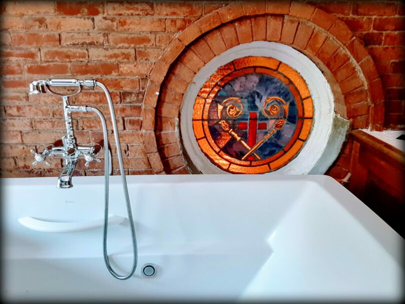 a clawfoot bathtub has stained glass behind it